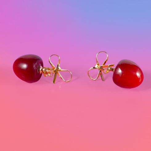 Gold bow earrings with dangling red cherry charms. Coquette-style jewelry perfect for soft girl and balletcore aesthetics. Handmade resin fruit earrings for summer style.