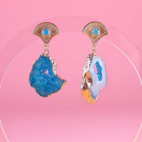 A pair of earrings featuring vibrant blue agate geode slices with natural crystal formations. Each earring has a 14k gold-plated fan-shaped post adorned with a small zircon rhinestone, combining earthy textures with Art Deco-inspired elegance.