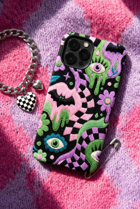 Dual layer phone case in matte or glossy with a 2D print that mimics thick crochet and yarn embroidery. Black bats, pink and green dripping slime, all-seeing eyes with lashes, purple and green daisies, and twisting pink and black checkered worms scatter across a black knit-look background. Smooth printed surface with no raised threads, open ports, and camera cutout. Pastel goth, creepy cute, whimsigoth, spooky maximalist phone accessory and gift.