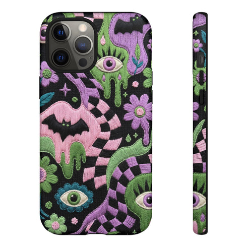 Dual layer phone case in matte or glossy with a 2D print that mimics thick crochet and yarn embroidery. Black bats, pink and green dripping slime, all-seeing eyes with lashes, purple and green daisies, and twisting pink and black checkered worms scatter across a black knit-look background. Smooth printed surface with no raised threads, open ports, and camera cutout. Pastel goth, creepy cute, whimsigoth, spooky maximalist phone accessory and gift.