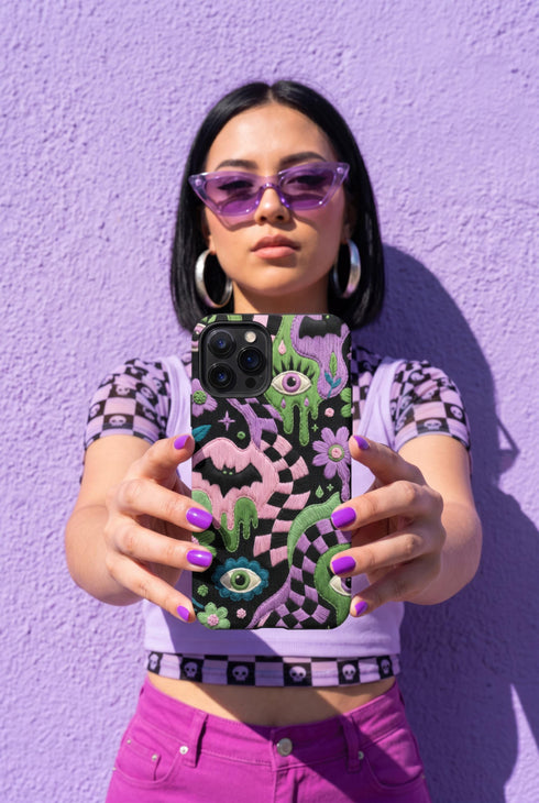 Dual layer phone case in matte or glossy with a 2D print that mimics thick crochet and yarn embroidery. Black bats, pink and green dripping slime, all-seeing eyes with lashes, purple and green daisies, and twisting pink and black checkered worms scatter across a black knit-look background. Smooth printed surface with no raised threads, open ports, and camera cutout. Pastel goth, creepy cute, whimsigoth, spooky maximalist phone accessory and gift.