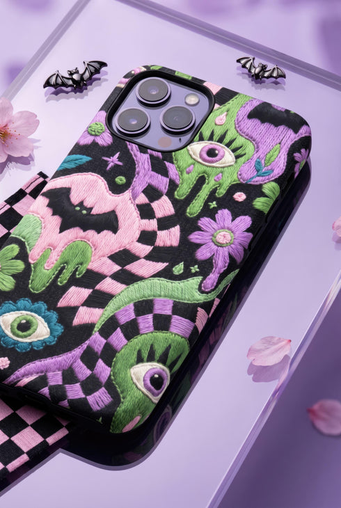 Dual layer phone case in matte or glossy with a 2D print that mimics thick crochet and yarn embroidery. Black bats, pink and green dripping slime, all-seeing eyes with lashes, purple and green daisies, and twisting pink and black checkered worms scatter across a black knit-look background. Smooth printed surface with no raised threads, open ports, and camera cutout. Pastel goth, creepy cute, whimsigoth, spooky maximalist phone accessory and gift.