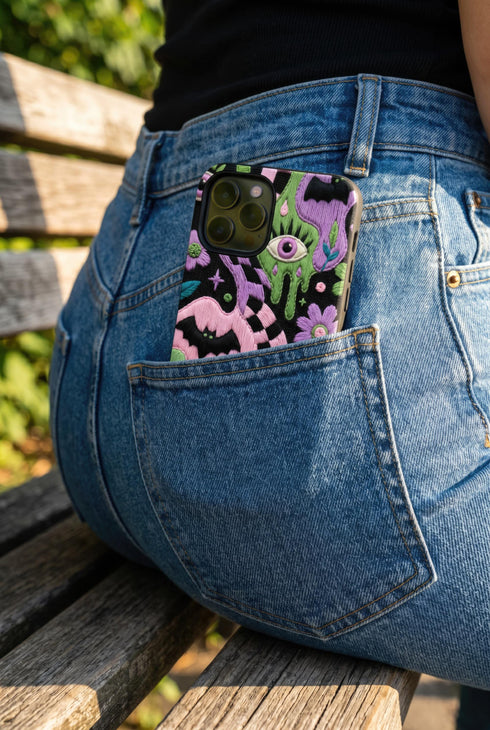 Dual layer phone case in matte or glossy with a 2D print that mimics thick crochet and yarn embroidery. Black bats, pink and green dripping slime, all-seeing eyes with lashes, purple and green daisies, and twisting pink and black checkered worms scatter across a black knit-look background. Smooth printed surface with no raised threads, open ports, and camera cutout. Pastel goth, creepy cute, whimsigoth, spooky maximalist phone accessory and gift.