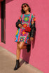 Short sleeve crew neck t-shirt dress in a relaxed, oversized straight cut, made of 100% polyester with a soft matte finish. An edge-to-edge all-over print shows 70s mod flowers in red, green, yellow, and purple set inside quilt-style patchwork panels of hot pink, royal blue, and lavender, divided by vertical stripes of red and pink polka dots. Retro 70s hippie, patchwork quilt, dopamine dressing maximalist alt fashion.