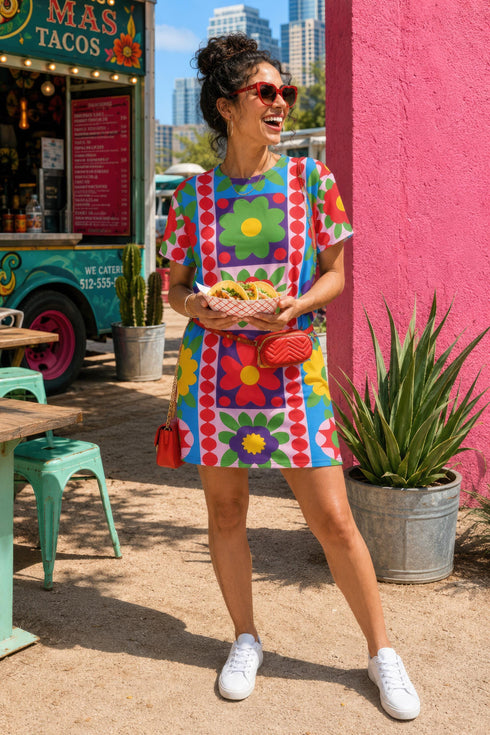 Short sleeve crew neck t-shirt dress in a relaxed, oversized straight cut, made of 100% polyester with a soft matte finish. An edge-to-edge all-over print shows 70s mod flowers in red, green, yellow, and purple set inside quilt-style patchwork panels of hot pink, royal blue, and lavender, divided by vertical stripes of red and pink polka dots. Retro 70s hippie, patchwork quilt, dopamine dressing maximalist alt fashion.