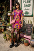Short sleeve crew neck t-shirt dress in a relaxed, oversized straight cut, made of 100% polyester with a soft matte finish. An edge-to-edge all-over print shows yellow radial sunburst medallions with jagged rays on a hot pink background, layered blue and pink circular centers, rows of small blue stars, a partial eye near the top, and dark charcoal swirling vine filigree along the hem. Psychedelic 70s retro, celestial, whimsigoth maximalist alt fashion.