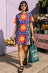 Short sleeve crew neck t-shirt dress in a relaxed, oversized straight cut, made of 100% polyester with a soft matte finish. An edge-to-edge all-over print on a medium purple background shows vertically stacked daisies with orange petals and yellow centers, scattered white four-point stars, and blue and green wavy side borders filled with small black and white daisies. Retro 70s floral, groovy maximalist alt fashion.