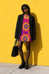 Short sleeve crew neck t-shirt dress in a relaxed, oversized straight cut, made of 100% polyester with a soft matte finish. An edge-to-edge all-over print shows yellow radial sunburst medallions with jagged rays on a hot pink background, layered blue and pink circular centers, rows of small blue stars, a partial eye near the top, and dark charcoal swirling vine filigree along the hem. Psychedelic 70s retro, celestial, whimsigoth maximalist alt fashion.