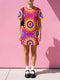 Short sleeve crew neck t-shirt dress in a relaxed, oversized straight cut, made of 100% polyester with a soft matte finish. An edge-to-edge all-over print shows yellow radial sunburst medallions with jagged rays on a hot pink background, layered blue and pink circular centers, rows of small blue stars, a partial eye near the top, and dark charcoal swirling vine filigree along the hem. Psychedelic 70s retro, celestial, whimsigoth maximalist alt fashion.