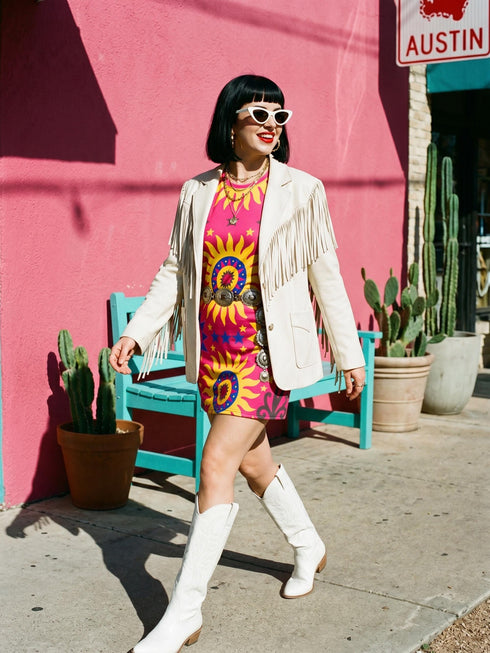 Short sleeve crew neck t-shirt dress in a relaxed, oversized straight cut, made of 100% polyester with a soft matte finish. An edge-to-edge all-over print shows yellow radial sunburst medallions with jagged rays on a hot pink background, layered blue and pink circular centers, rows of small blue stars, a partial eye near the top, and dark charcoal swirling vine filigree along the hem. Psychedelic 70s retro, celestial, whimsigoth maximalist alt fashion.