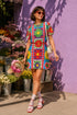 Short sleeve crew neck t-shirt dress in a relaxed, oversized straight cut, made of 100% polyester with a soft matte finish. An edge-to-edge all-over print shows 70s mod flowers in red, green, yellow, and purple set inside quilt-style patchwork panels of hot pink, royal blue, and lavender, divided by vertical stripes of red and pink polka dots. Retro 70s hippie, patchwork quilt, dopamine dressing maximalist alt fashion.