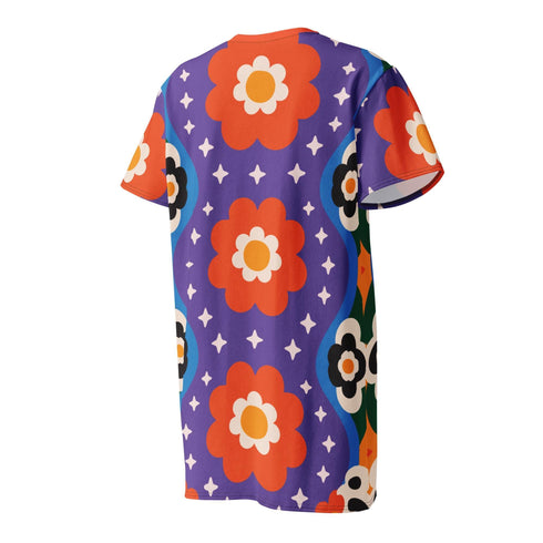Short sleeve crew neck t-shirt dress in a relaxed, oversized straight cut, made of 100% polyester with a soft matte finish. An edge-to-edge all-over print on a medium purple background shows vertically stacked daisies with orange petals and yellow centers, scattered white four-point stars, and blue and green wavy side borders filled with small black and white daisies. Retro 70s floral, groovy maximalist alt fashion.