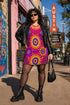 Short sleeve crew neck t-shirt dress in a relaxed, oversized straight cut, made of 100% polyester with a soft matte finish. An edge-to-edge all-over print shows yellow radial sunburst medallions with jagged rays on a hot pink background, layered blue and pink circular centers, rows of small blue stars, a partial eye near the top, and dark charcoal swirling vine filigree along the hem. Psychedelic 70s retro, celestial, whimsigoth maximalist alt fashion.