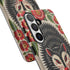 Dual layer matte phone case with a 2D print that mimics thick crewel embroidery. An angry black possum with a white face, bared sharp teeth, and bright red eyes and claws sits at the center on a cream background, framed by a symmetrical border of red folk art daisies with yellow centers and green leaves. Smooth printed surface with no raised threads, open ports, and a precise camera cutout. Goblincore, creepy cute, maximalist phone accessory.