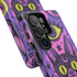 Dual layer matte phone case with a 2D print that mimics raised embroidery. Dark purple vampire bat cat heads with tall pointed ears, glowing chartreuse eyes, tiny fangs, and a pink crescent moon on the forehead repeat across a mottled purple and hot pink background, scattered with large chartreuse evil eyes with purple irises and small dark stars. Smooth printed surface with no raised threads, open ports, and camera cutout. Pastel goth, whimsigoth, creepy cute phone accessory.