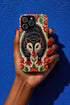 Dual layer matte phone case with a 2D print that mimics thick crewel embroidery. An angry black possum with a white face, bared sharp teeth, and bright red eyes and claws sits at the center on a cream background, framed by a symmetrical border of red folk art daisies with yellow centers and green leaves. Smooth printed surface with no raised threads, open ports, and a precise camera cutout. Goblincore, creepy cute, maximalist phone accessory.