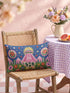 Rectangular 20 by 12 inch lumbar pillow cover printed to look like thick crewel embroidery on a deep royal blue night sky dotted with orange, yellow, and white stars. A silver, pink, and yellow flying saucer beams a bright pink cone of light onto a white cow with green spots standing in green grass with pine trees and red and pink flowers. Smooth flat 2D print, not raised stitching. Maximalist sci-fi decor for a bed, sofa, or reading nook.
