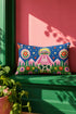 Rectangular 20 by 12 inch lumbar pillow cover printed to look like thick crewel embroidery on a deep royal blue night sky dotted with orange, yellow, and white stars. A silver, pink, and yellow flying saucer beams a bright pink cone of light onto a white cow with green spots standing in green grass with pine trees and red and pink flowers. Smooth flat 2D print, not raised stitching. Maximalist sci-fi decor for a bed, sofa, or reading nook.