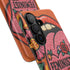 Dual layer matte phone case with a 2D print that mimics knit and embroidery texture. A retro open mouth with its tongue out sits over a pink heart stitched with the word FEMINIST in black letters, on an orange knit-look background filled with pink flowers, yellow sunflowers, red roses, purple and orange blooms, teal leaves, and a turquoise drip, all outlined in bold black. Smooth printed surface, open ports, camera cutout. Feminist maximalist phone accessory.