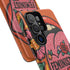 Dual layer matte phone case with a 2D print that mimics knit and embroidery texture. A retro open mouth with its tongue out sits over a pink heart stitched with the word FEMINIST in black letters, on an orange knit-look background filled with pink flowers, yellow sunflowers, red roses, purple and orange blooms, teal leaves, and a turquoise drip, all outlined in bold black. Smooth printed surface, open ports, camera cutout. Feminist maximalist phone accessory.
