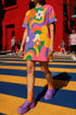 Short sleeve crew neck t-shirt dress in a relaxed, oversized straight cut, made of 100% polyester with a soft matte finish. An edge-to-edge all-over print shows pop-art daisies in cream, yellow, orange, and purple layered over wavy psychedelic stripes of hot pink, kelly green, orange, purple, and yellow. Retro 60s mod, flower power, psychedelic pop art, dopamine dressing maximalist alt fashion for festivals.