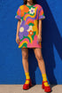 Short sleeve crew neck t-shirt dress in a relaxed, oversized straight cut, made of 100% polyester with a soft matte finish. An edge-to-edge all-over print shows pop-art daisies in cream, yellow, orange, and purple layered over wavy psychedelic stripes of hot pink, kelly green, orange, purple, and yellow. Retro 60s mod, flower power, psychedelic pop art, dopamine dressing maximalist alt fashion for festivals.