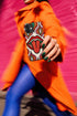 Dual layer matte phone case with a 2D print that mimics heavy crochet and thick knit yarn. A large open mouth with bright red lips and a red tongue sticking out sits at the center of a cream background, surrounded by mirrored teardrop and flame shapes in bright orange, dark green, and hot pink with black stitch-style outlines. Smooth printed surface with no raised threads, open ports, and camera cutout. Psychedelic 70s pop art phone accessory.