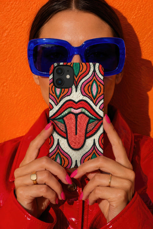Dual layer matte phone case with a 2D print that mimics heavy crochet and thick knit yarn. A large open mouth with bright red lips and a red tongue sticking out sits at the center of a cream background, surrounded by mirrored teardrop and flame shapes in bright orange, dark green, and hot pink with black stitch-style outlines. Smooth printed surface with no raised threads, open ports, and camera cutout. Psychedelic 70s pop art phone accessory.