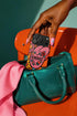 Dual layer matte phone case with a 2D print that mimics knit and embroidery texture. A retro open mouth with its tongue out sits over a pink heart stitched with the word FEMINIST in black letters, on an orange knit-look background filled with pink flowers, yellow sunflowers, red roses, purple and orange blooms, teal leaves, and a turquoise drip, all outlined in bold black. Smooth printed surface, open ports, camera cutout. Feminist maximalist phone accessory.