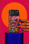 Dual layer matte phone case with a 2D print that mimics knit and embroidery texture. A retro open mouth with its tongue out sits over a pink heart stitched with the word FEMINIST in black letters, on an orange knit-look background filled with pink flowers, yellow sunflowers, red roses, purple and orange blooms, teal leaves, and a turquoise drip, all outlined in bold black. Smooth printed surface, open ports, camera cutout. Feminist maximalist phone accessory.