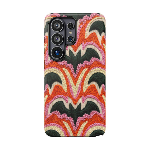 Dual layer matte phone case with a 2D print that mimics thick, heavy crochet yarn. Rows of stacked black bats repeat across a vibrant rust-orange background, accented with bright pink faux yarn bobbles and framed by cream arched lines. Smooth printed surface with no raised threads, open ports, and a precise camera cutout. Pastel goth, creepy cute, Summerween and Halloween phone accessory with a cozy handmade look.