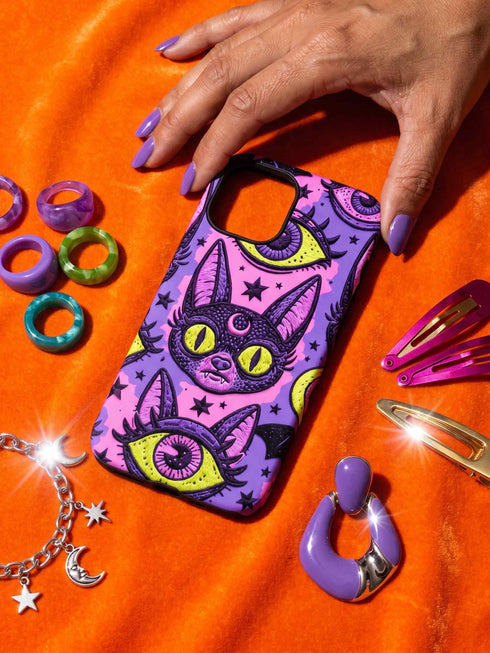Dual layer matte phone case with a 2D print that mimics raised embroidery. Dark purple vampire bat cat heads with tall pointed ears, glowing chartreuse eyes, tiny fangs, and a pink crescent moon on the forehead repeat across a mottled purple and hot pink background, scattered with large chartreuse evil eyes with purple irises and small dark stars. Smooth printed surface with no raised threads, open ports, and camera cutout. Pastel goth, whimsigoth, creepy cute phone accessory.