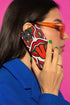 Dual layer matte phone case with a 2D print that mimics heavy crochet and thick knit yarn. A large open mouth with bright red lips and a red tongue sticking out sits at the center of a cream background, surrounded by mirrored teardrop and flame shapes in bright orange, dark green, and hot pink with black stitch-style outlines. Smooth printed surface with no raised threads, open ports, and camera cutout. Psychedelic 70s pop art phone accessory.