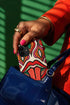 Dual layer matte phone case with a 2D print that mimics heavy crochet and thick knit yarn. A large open mouth with bright red lips and a red tongue sticking out sits at the center of a cream background, surrounded by mirrored teardrop and flame shapes in bright orange, dark green, and hot pink with black stitch-style outlines. Smooth printed surface with no raised threads, open ports, and camera cutout. Psychedelic 70s pop art phone accessory.