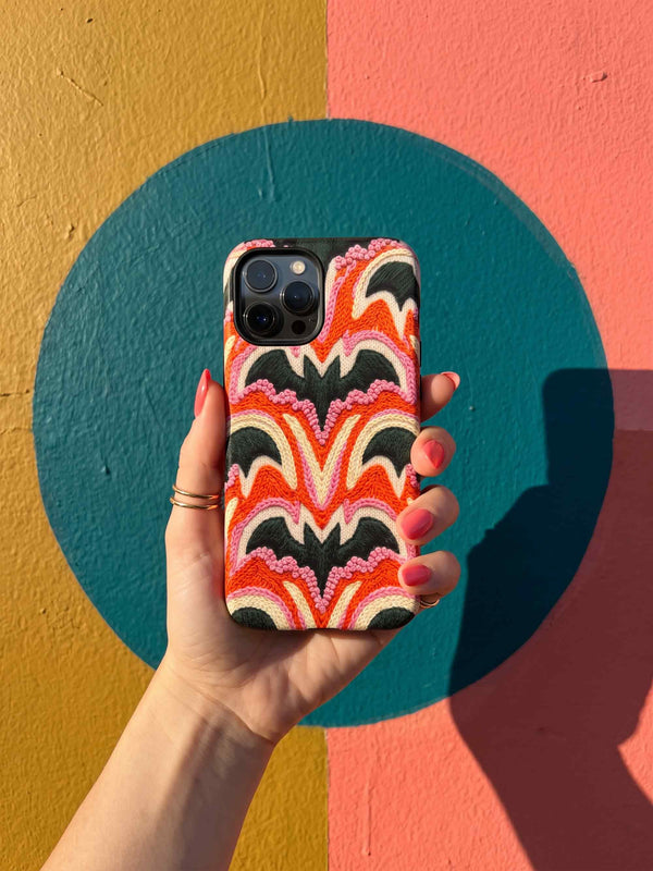 Dual layer matte phone case with a 2D print that mimics thick, heavy crochet yarn. Rows of stacked black bats repeat across a vibrant rust-orange background, accented with bright pink faux yarn bobbles and framed by cream arched lines. Smooth printed surface with no raised threads, open ports, and a precise camera cutout. Pastel goth, creepy cute, Summerween and Halloween phone accessory with a cozy handmade look.