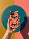 Dual layer matte phone case with a 2D print that mimics thick, heavy crochet yarn. Rows of stacked black bats repeat across a vibrant rust-orange background, accented with bright pink faux yarn bobbles and framed by cream arched lines. Smooth printed surface with no raised threads, open ports, and a precise camera cutout. Pastel goth, creepy cute, Summerween and Halloween phone accessory with a cozy handmade look.