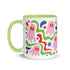 Glossy white ceramic 11 oz coffee mug with a lime green rim, inside, and handle and a full wraparound pastel goth print. Pink ghosts with paired red oval eyes and rounded scalloped lower edges float between wavy green and red ribbons. Blue starbursts, curved blue shapes, red teardrops, small colorful dots, and green diamond sparkles fill the white background. Creepy cute Halloween coffee mug with a playful, retro maximalist feel.
