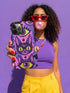 Dual layer matte phone case with a 2D print that mimics raised embroidery. Dark purple vampire bat cat heads with tall pointed ears, glowing chartreuse eyes, tiny fangs, and a pink crescent moon on the forehead repeat across a mottled purple and hot pink background, scattered with large chartreuse evil eyes with purple irises and small dark stars. Smooth printed surface with no raised threads, open ports, and camera cutout. Pastel goth, whimsigoth, creepy cute phone accessory.