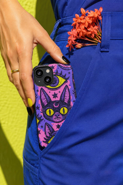 Dual layer matte phone case with a 2D print that mimics raised embroidery. Dark purple vampire bat cat heads with tall pointed ears, glowing chartreuse eyes, tiny fangs, and a pink crescent moon on the forehead repeat across a mottled purple and hot pink background, scattered with large chartreuse evil eyes with purple irises and small dark stars. Smooth printed surface with no raised threads, open ports, and camera cutout. Pastel goth, whimsigoth, creepy cute phone accessory.