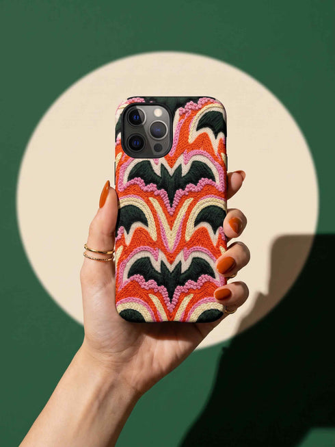 Dual layer matte phone case with a 2D print that mimics thick, heavy crochet yarn. Rows of stacked black bats repeat across a vibrant rust-orange background, accented with bright pink faux yarn bobbles and framed by cream arched lines. Smooth printed surface with no raised threads, open ports, and a precise camera cutout. Pastel goth, creepy cute, Summerween and Halloween phone accessory with a cozy handmade look.
