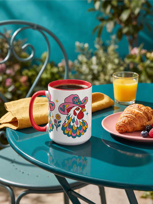 Glossy white ceramic coffee mug with a colored rim, inside, and handle and a full wraparound folk art print. Chickens wear pink cowboy hats with teal bands, yellow diamonds, flowers, and teardrop motifs. The birds have white heads, red combs and wattles, and layered pink, teal, and golden yellow feathers outlined in black. Pink and yellow flowers, teal leaves, and four-point starbursts fill the space between. Retro western kitchen decor.