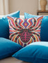Square psychedelic folk art throw pillow cover printed to look like textured embroidery on a cream background. A large black spider with coral red and magenta markings on its legs and abdomen sits at the center, surrounded by rippling waves in blue violet, coral red, magenta, and golden yellow. Smooth flat 2D print, not raised stitching. Retro gothic Halloween maximalist decor for a sofa, armchair, or goth bedroom, made for spooky season.