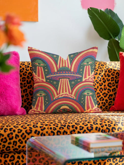 Square 70s psychedelic throw pillow cover printed to look like textured embroidery on a dark, starry navy background. Retro flying saucers and stylized alien eyes repeat across the design above rainbow arches, with small yellow stars and beams of light. Smooth flat 2D print, not raised stitching. Trippy, groovy, retro space age maximalist decor for a sofa, dorm bed, or reading nook, made for sci-fi fans and alien lovers.