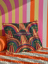Square 70s psychedelic throw pillow cover printed to look like textured embroidery on a dark, starry navy background. Retro flying saucers and stylized alien eyes repeat across the design above rainbow arches, with small yellow stars and beams of light. Smooth flat 2D print, not raised stitching. Trippy, groovy, retro space age maximalist decor for a sofa, dorm bed, or reading nook, made for sci-fi fans and alien lovers.