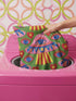 Square weirdcore throw pillow cover printed to look like textured crewel embroidery on a green background. A pink and blue flying saucer with one large blue eye at its center hovers among floating blue eyeballs and red hearts. Smooth flat 2D print, not raised stitching. Maximalist, trippy sci-fi dopamine decor with quirky alien charm for a sofa, dorm bed, gaming chair, or reading nook, made for space lovers and sci-fi fans.