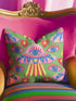 Square weirdcore throw pillow cover printed to look like textured crewel embroidery on a green background. A pink and blue flying saucer with one large blue eye at its center hovers among floating blue eyeballs and red hearts. Smooth flat 2D print, not raised stitching. Maximalist, trippy sci-fi dopamine decor with quirky alien charm for a sofa, dorm bed, gaming chair, or reading nook, made for space lovers and sci-fi fans.