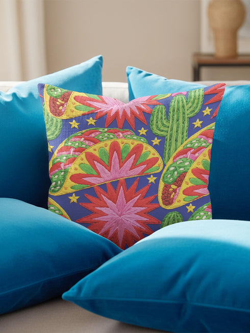 Square maximalist throw pillow cover printed to look like bold crewel embroidery on a solid royal blue background. Tacos with green, red, and brown fillings scatter across the design with bright green saguaro cacti, large pink and red starburst flowers, and small yellow stars. Smooth flat 2D print, not raised stitching. Colorful, quirky dopamine decor for a sofa, kitchen bench, or breakfast nook, made for taco lovers and foodies.