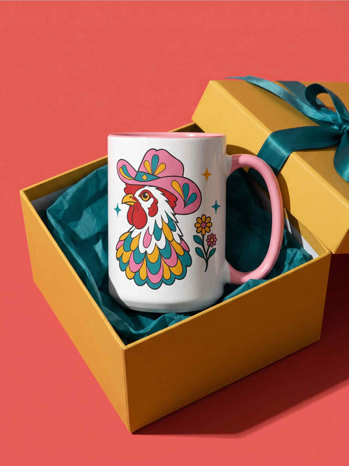 Glossy white ceramic coffee mug with a colored rim, inside, and handle and a full wraparound folk art print. Chickens wear pink cowboy hats with teal bands, yellow diamonds, flowers, and teardrop motifs. The birds have white heads, red combs and wattles, and layered pink, teal, and golden yellow feathers outlined in black. Pink and yellow flowers, teal leaves, and four-point starbursts fill the space between. Retro western kitchen decor.