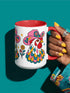 Glossy white ceramic coffee mug with a colored rim, inside, and handle and a full wraparound folk art print. Chickens wear pink cowboy hats with teal bands, yellow diamonds, flowers, and teardrop motifs. The birds have white heads, red combs and wattles, and layered pink, teal, and golden yellow feathers outlined in black. Pink and yellow flowers, teal leaves, and four-point starbursts fill the space between. Retro western kitchen decor.