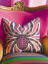 Square psychedelic folk art throw pillow cover printed to look like textured embroidery on a cream background. A large black spider with coral red and magenta markings on its legs and abdomen sits at the center, surrounded by rippling waves in blue violet, coral red, magenta, and golden yellow. Smooth flat 2D print, not raised stitching. Retro gothic Halloween maximalist decor for a sofa, armchair, or goth bedroom, made for spooky season.